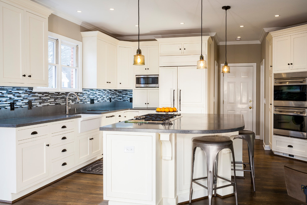 Eat-in kitchen - large transitional l-shaped medium tone wood floor and brown floor eat-in kitchen idea in Atlanta with a farmhouse sink, shaker cabinets, white cabinets, solid surface countertops, multicolored backsplash, glass sheet backsplash, paneled appliances and an island