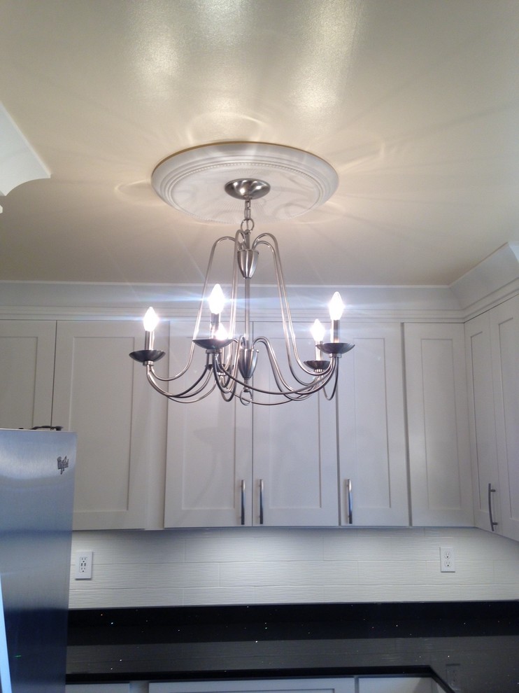 Mid-sized arts and crafts u-shaped vinyl floor home design photo with a double-bowl sink, shaker cabinets, white cabinets, quartz countertops, white backsplash, porcelain backsplash, stainless steel appliances and no island