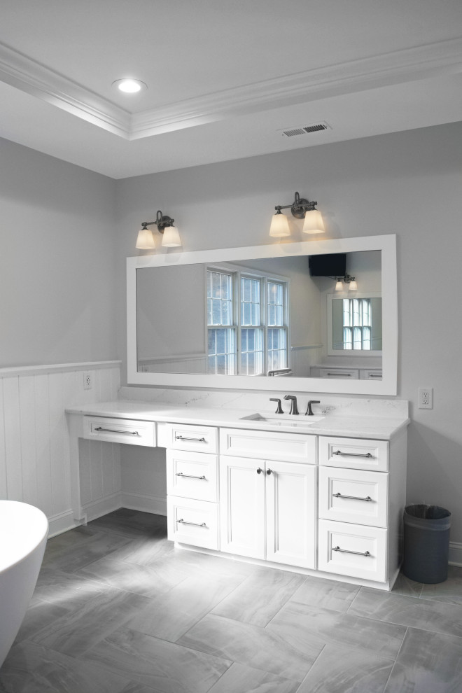 Photo of a large classic ensuite bathroom in Philadelphia with recessed-panel cabinets, white cabinets, a freestanding bath, a double shower, a one-piece toilet, grey tiles, ceramic tiles, grey walls, porcelain flooring, a submerged sink, engineered stone worktops, grey floors, a hinged door, white worktops, a wall niche, double sinks, a built in vanity unit, a drop ceiling and wainscoting.