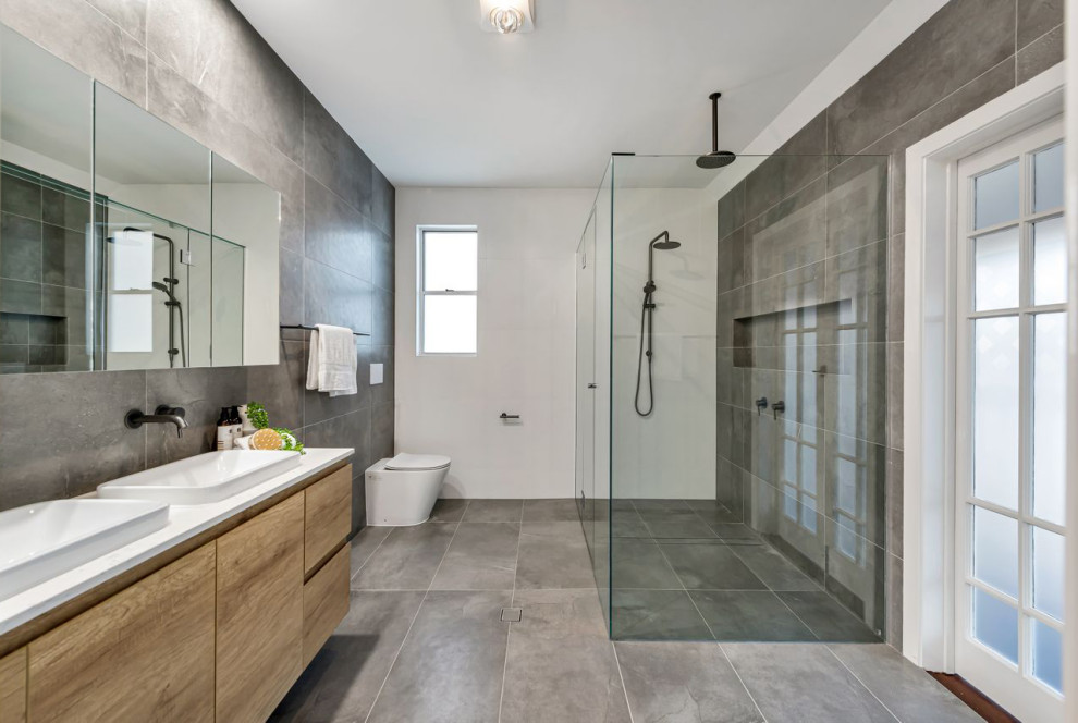 This is an example of a mid-sized contemporary 3/4 bathroom in Brisbane with flat-panel cabinets, beige cabinets, a corner shower, a wall-mount toilet, gray tile, porcelain tile, white walls, porcelain floors, a vessel sink, grey floor, a hinged shower door and white benchtops.