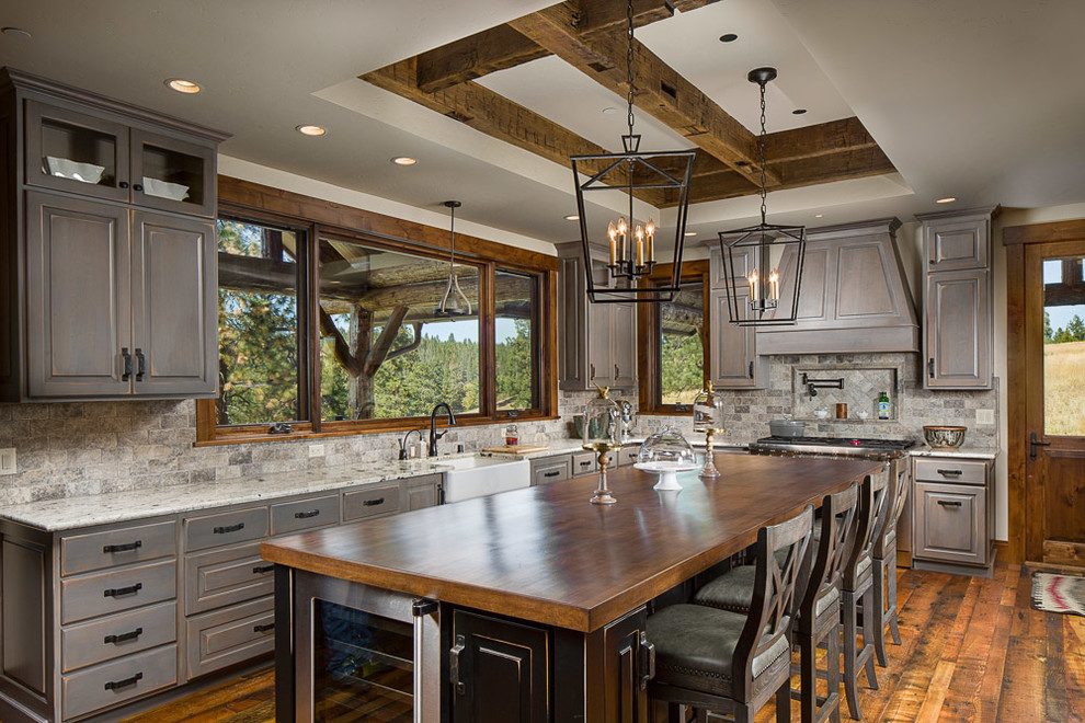 Example of a large mountain style l-shaped dark wood floor kitchen design with a farmhouse sink, raised-panel cabinets, distressed cabinets, brown backsplash, paneled appliances, an island and wood countertops