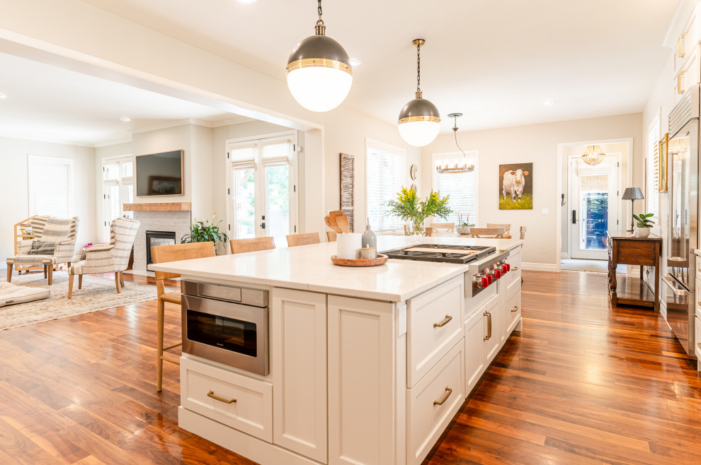 Open concept kitchen - large transitional l-shaped dark wood floor and brown floor open concept kitchen idea in Denver with a farmhouse sink, shaker cabinets, beige cabinets, quartz countertops, beige backsplash, ceramic backsplash, stainless steel appliances, an island and white countertops
