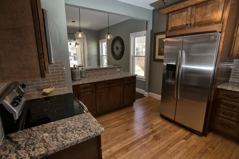 This is an example of a small arts and crafts u-shaped eat-in kitchen in Cleveland with an undermount sink, shaker cabinets, medium wood cabinets, granite benchtops, beige splashback, subway tile splashback, stainless steel appliances and light hardwood floors.