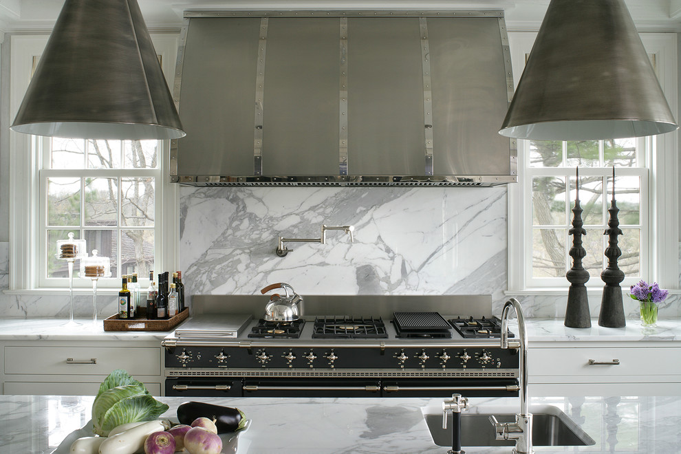 Example of a large transitional dark wood floor and brown floor enclosed kitchen design in New York with an undermount sink, flat-panel cabinets, white cabinets, marble countertops, white backsplash, marble backsplash, black appliances and an island