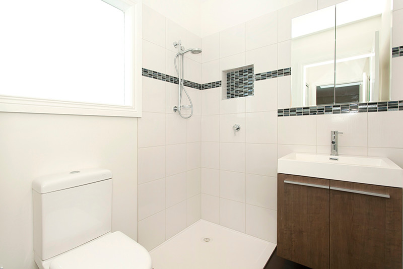 Inspiration for a small modern bathroom in Melbourne with an integrated sink, flat-panel cabinets, dark wood cabinets, engineered quartz benchtops, a corner shower, a one-piece toilet, white tile, ceramic tile and white walls.