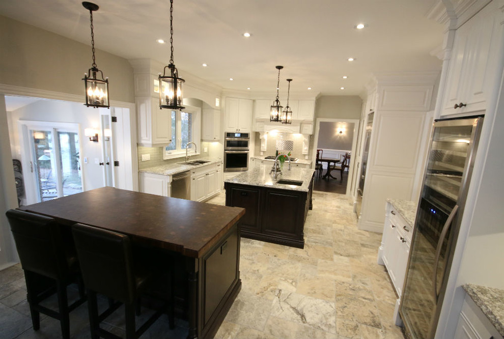 Photo of an expansive traditional u-shaped kitchen in Toronto with an undermount sink, raised-panel cabinets, white cabinets, quartz benchtops, beige splashback, glass tile splashback, stainless steel appliances and multiple islands.