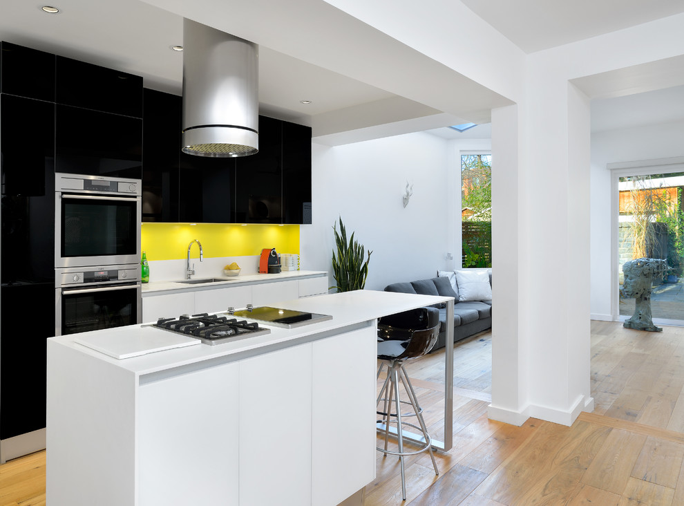 Inspiration for a modern galley open plan kitchen in Toronto with an undermount sink, flat-panel cabinets, black cabinets, yellow splashback, quartzite benchtops, stainless steel appliances, light hardwood floors and with island.