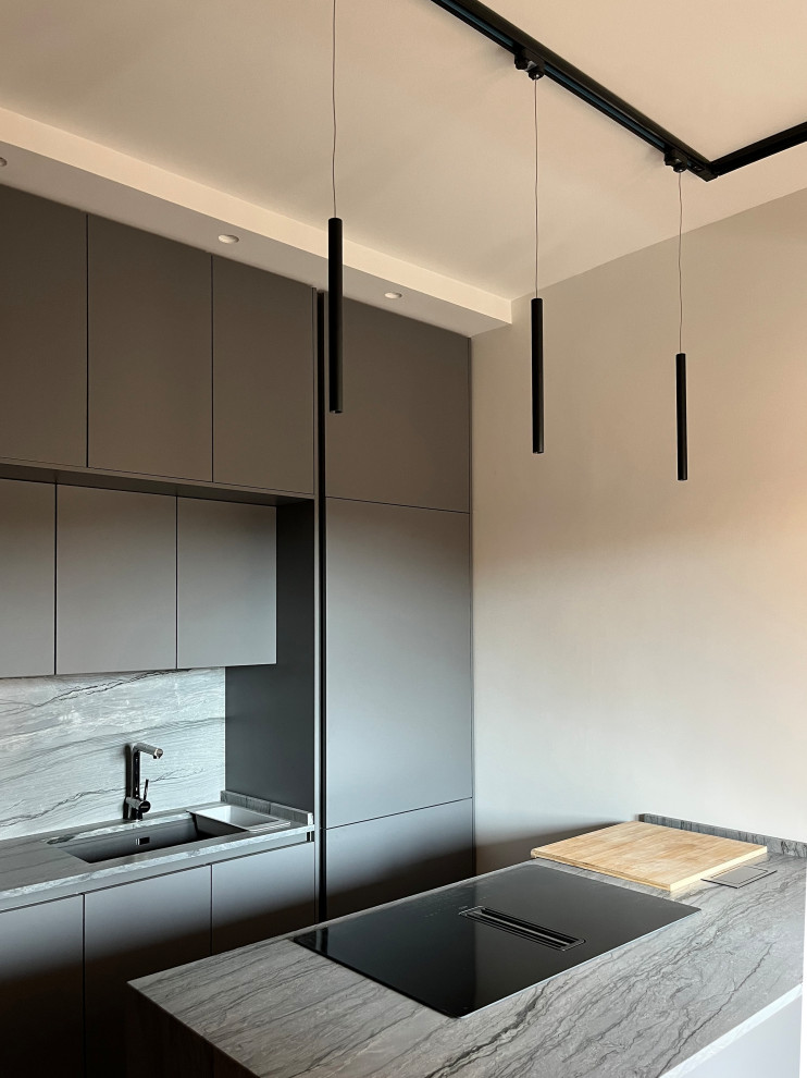 Bild på ett mellanstort funkis grå grått kök, med en integrerad diskho, släta luckor, grå skåp, bänkskiva i kalksten, grått stänkskydd, stänkskydd i kalk, svarta vitvaror, ljust trägolv, en köksö och brunt golv