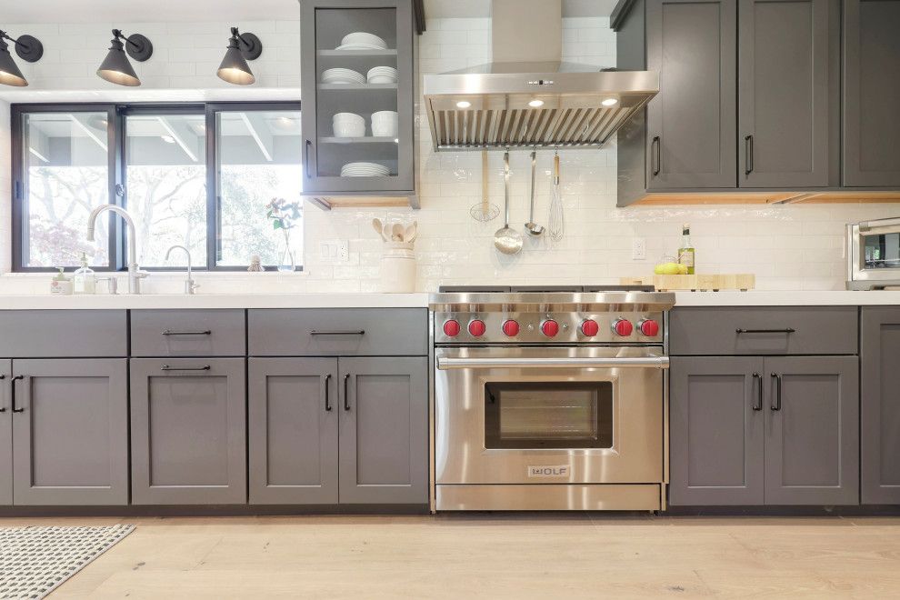 Open concept kitchen - mid-sized transitional l-shaped laminate floor open concept kitchen idea with a double-bowl sink, flat-panel cabinets, gray cabinets, quartz countertops, white backsplash, ceramic backsplash, stainless steel appliances, an island and white countertops