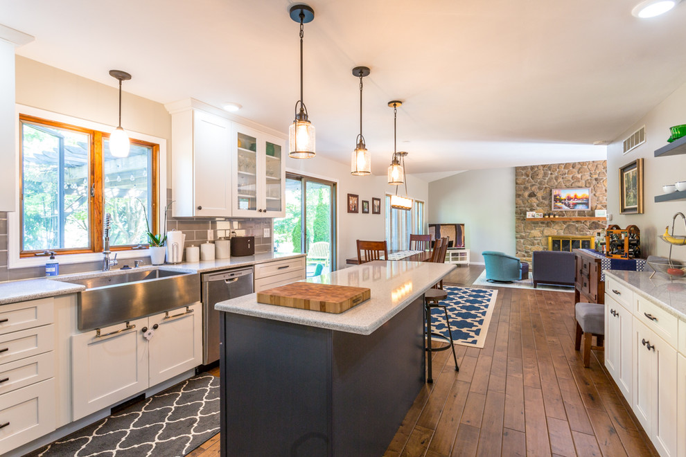 This is an example of a transitional u-shaped eat-in kitchen in Indianapolis with a farmhouse sink, shaker cabinets, white cabinets, grey splashback, subway tile splashback, stainless steel appliances, medium hardwood floors and with island.