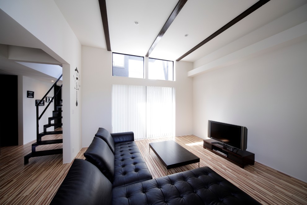 This is an example of a modern living room in Fukuoka with white walls, plywood floors and a freestanding tv.
