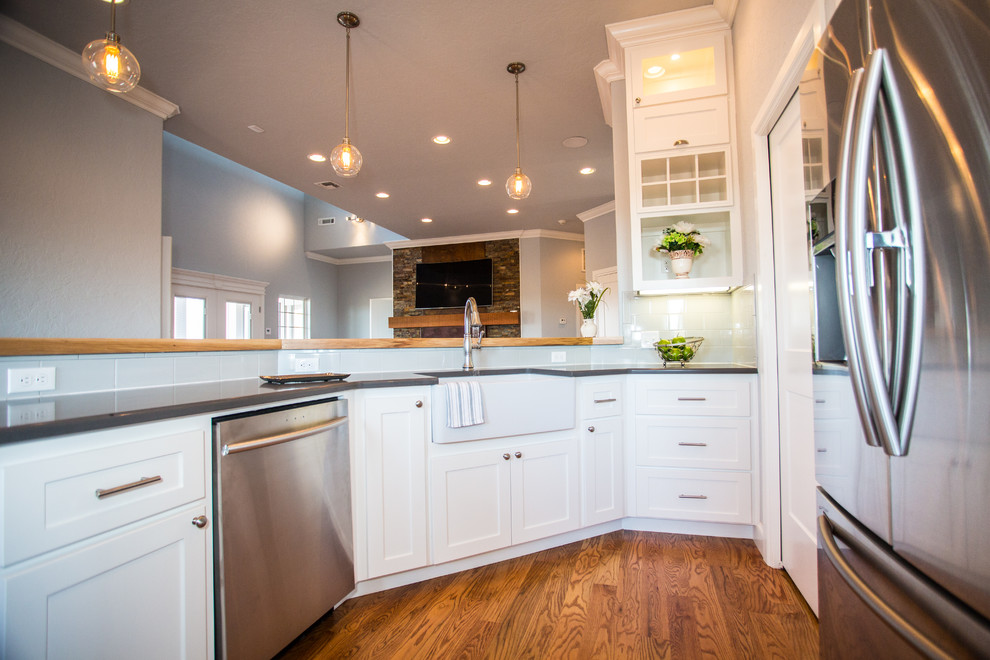 Example of a mid-sized transitional u-shaped medium tone wood floor and brown floor kitchen design in Orange County with a farmhouse sink, stainless steel appliances, white cabinets, gray backsplash, glass tile backsplash, shaker cabinets, solid surface countertops and no island