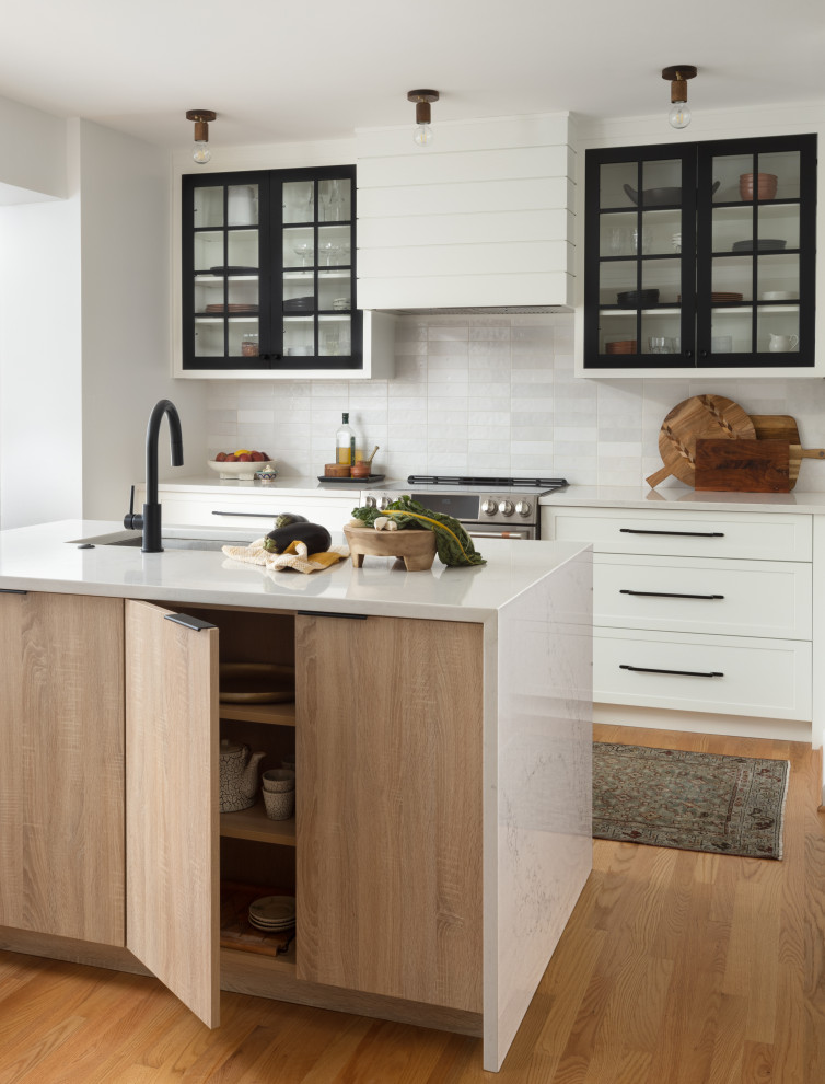 Photo of a small modern l-shaped kitchen/diner in DC Metro with a submerged sink, shaker cabinets, black cabinets, engineered stone countertops, grey splashback, ceramic splashback, stainless steel appliances, light hardwood flooring, an island, brown floors and white worktops.