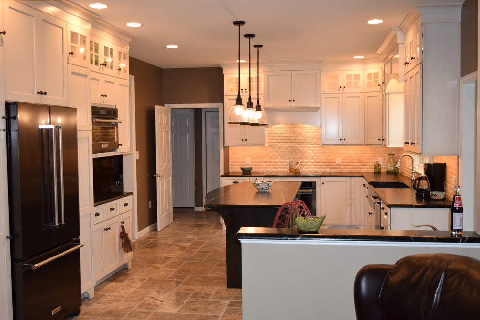 Example of a transitional l-shaped ceramic tile kitchen design with an undermount sink, shaker cabinets, white cabinets, quartz countertops, beige backsplash, subway tile backsplash, black appliances and an island