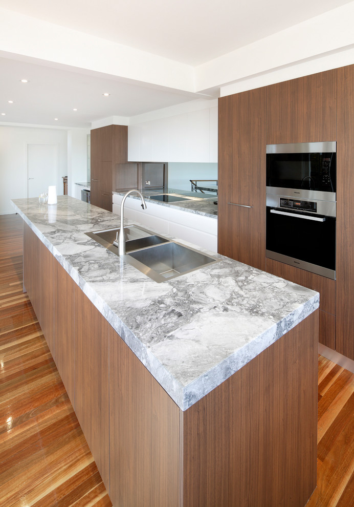 This is an example of a contemporary galley eat-in kitchen in Sydney with marble benchtops, metallic splashback, mirror splashback, stainless steel appliances, medium hardwood floors and with island.