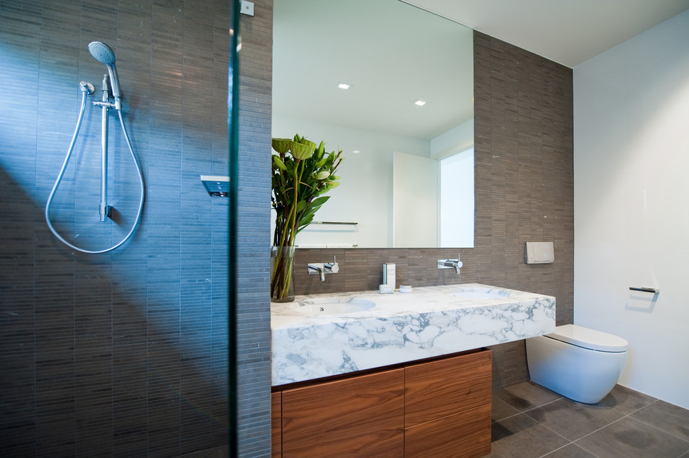 Photo of a small contemporary master bathroom in Adelaide with an undermount sink, flat-panel cabinets, medium wood cabinets, marble benchtops, an alcove shower, a one-piece toilet, brown tile, porcelain tile, brown walls and porcelain floors.