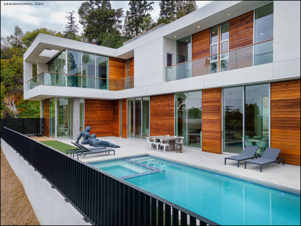 Modern back rectangular lengths swimming pool in Los Angeles with with pool landscaping and concrete paving.