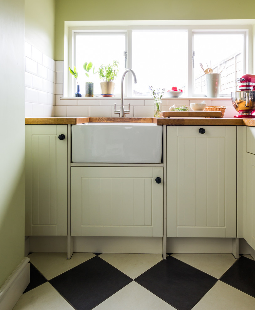 Small traditional l-shaped separate kitchen in Essex with a farmhouse sink, shaker cabinets, white cabinets, wood benchtops, white splashback, ceramic splashback, ceramic floors and no island.