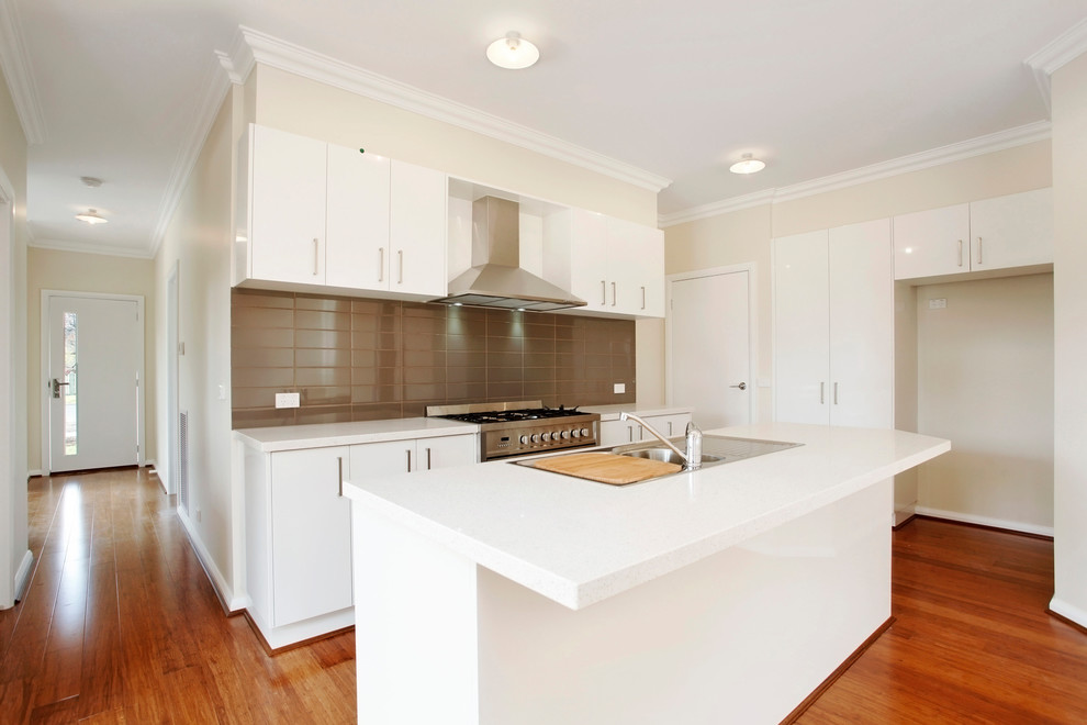 Inspiration for a mid-sized modern galley open plan kitchen in Melbourne with a drop-in sink, flat-panel cabinets, white cabinets, quartz benchtops, brown splashback, ceramic splashback, stainless steel appliances, bamboo floors, with island and brown floor.