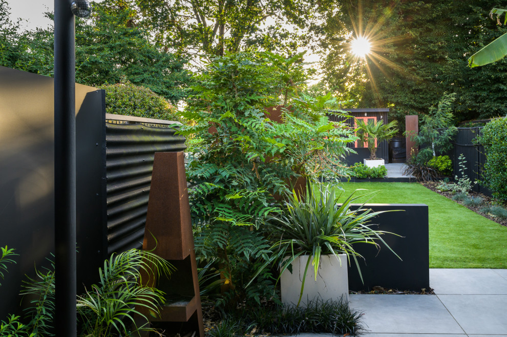 Inspiration for a mid-sized contemporary backyard partial sun garden in London with a fire feature, natural stone pavers and a metal fence.