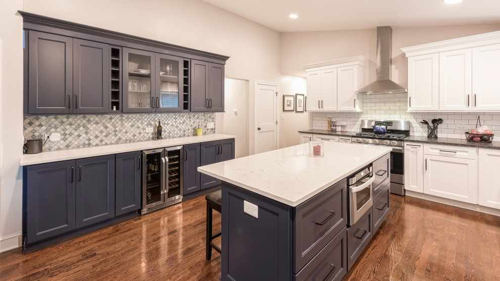 This is an example of a mid-sized traditional l-shaped eat-in kitchen in Chicago with a double-bowl sink, shaker cabinets, white cabinets, quartz benchtops, white splashback, subway tile splashback, stainless steel appliances, medium hardwood floors, with island, brown floor and white benchtop.