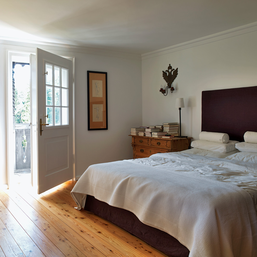 Country master bedroom in Munich with white walls, medium hardwood floors and no fireplace.