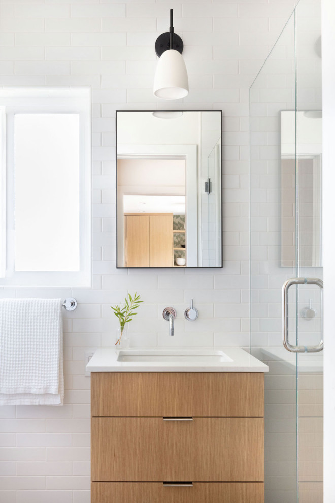 Cette image montre une petite salle de bain design en bois clair avec un placard à porte plane, une douche, tous types de WC, un carrelage blanc, des carreaux de céramique, un mur blanc, un sol en carrelage de porcelaine, un lavabo encastré, un plan de toilette en quartz modifié, un sol gris, une cabine de douche à porte battante, un plan de toilette blanc et meuble simple vasque.