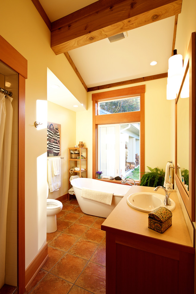 Mid-sized country master bathroom in Vancouver with a drop-in sink, shaker cabinets, medium wood cabinets, solid surface benchtops, a freestanding tub, an open shower, a one-piece toilet, multi-coloured tile, terra-cotta tile, white walls and terra-cotta floors.