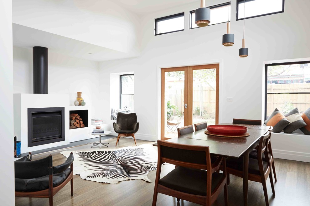 Photo of a modern open plan dining in Melbourne with white walls, medium hardwood floors, a standard fireplace and a metal fireplace surround.