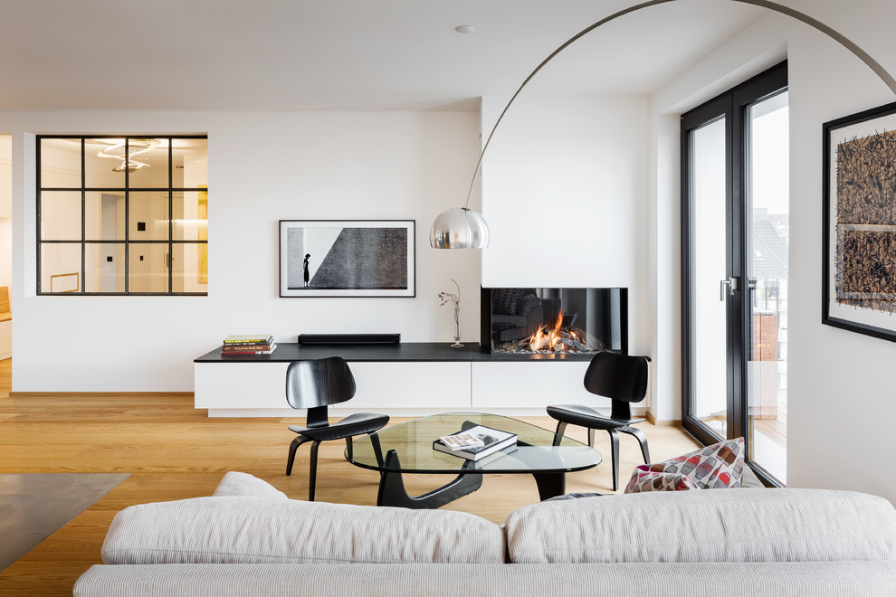 Inspiration for a mid-sized contemporary open concept family room in Essen with white walls, light hardwood floors, a ribbon fireplace, a wall-mounted tv, brown floor and a plaster fireplace surround.