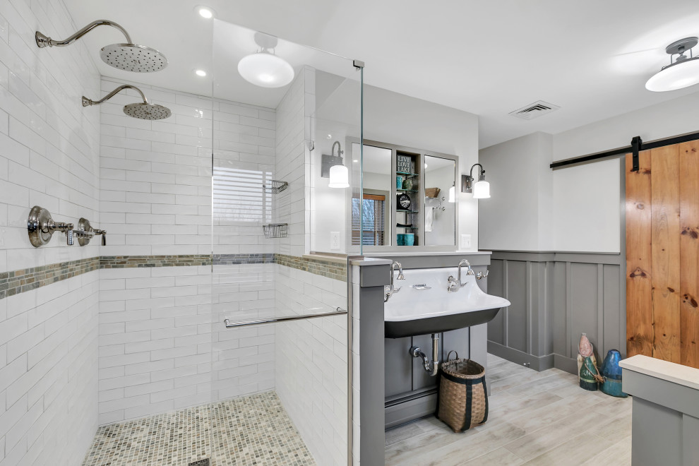 Bild på ett mellanstort amerikanskt en-suite badrum, med ett platsbyggt badkar, en dubbeldusch, en toalettstol med separat cisternkåpa, vit kakel, cementkakel, grå väggar, ett avlångt handfat, beiget golv och dusch med gångjärnsdörr