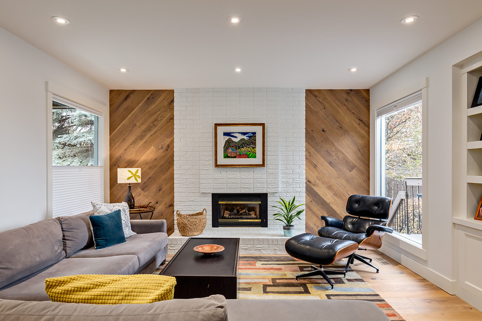 Large midcentury formal enclosed living room in Calgary with white walls, medium hardwood floors, a standard fireplace, a brick fireplace surround, no tv and beige floor.