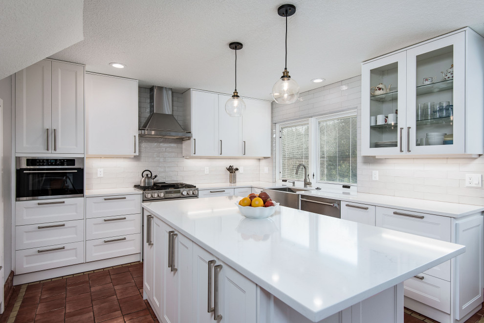 Photo of a mid-sized contemporary u-shaped eat-in kitchen in Portland with shaker cabinets, white cabinets, with island, a farmhouse sink, white splashback, ceramic splashback, stainless steel appliances, terra-cotta floors, red floor and white benchtop.