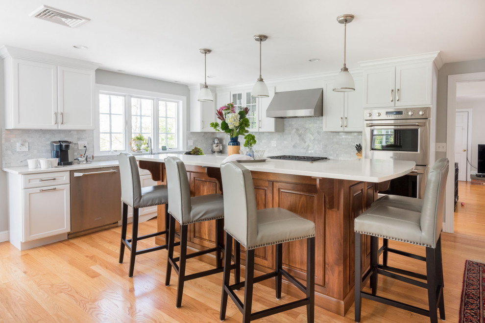 Example of a large transitional l-shaped medium tone wood floor, brown floor and coffered ceiling eat-in kitchen design in Boston with an undermount sink, shaker cabinets, white cabinets, quartz countertops, gray backsplash, subway tile backsplash, stainless steel appliances, an island and white countertops