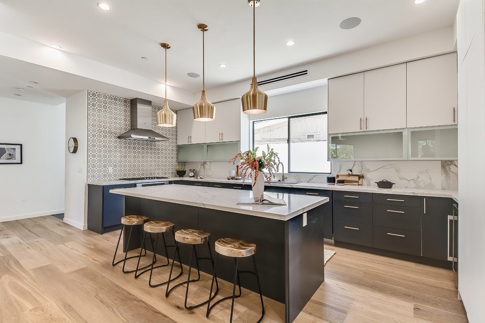 Large beach style u-shaped open plan kitchen in Los Angeles with flat-panel cabinets, blue cabinets, granite benchtops, multi-coloured splashback, stainless steel appliances, light hardwood floors, with island, brown floor and multi-coloured benchtop.