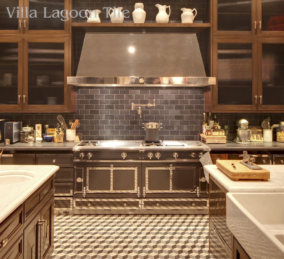 Expansive traditional single-wall kitchen in Los Angeles with a farmhouse sink, marble benchtops, black splashback, slate splashback, black appliances, cement tiles, multiple islands, multi-coloured floor, glass-front cabinets and dark wood cabinets.