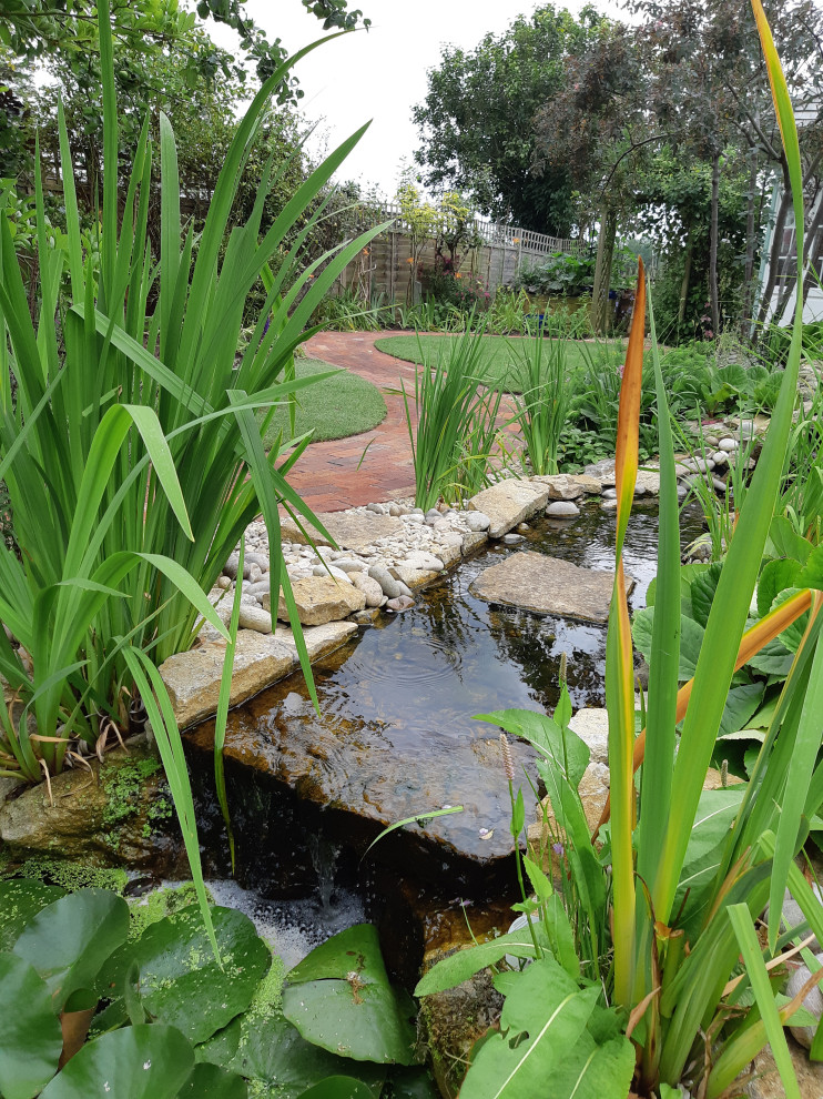 Photo of a mid-sized country backyard garden in Oxfordshire with with pond and river rock.