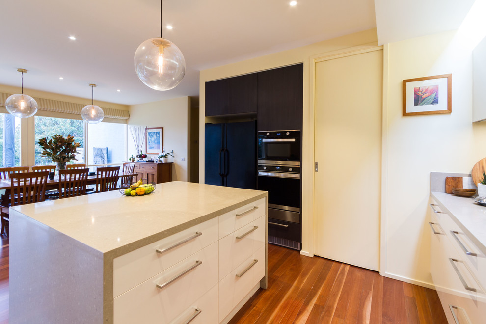 Design ideas for a large contemporary u-shaped open plan kitchen in Melbourne with flat-panel cabinets, quartz benchtops, black splashback, subway tile splashback, medium hardwood floors, with island and grey benchtop.