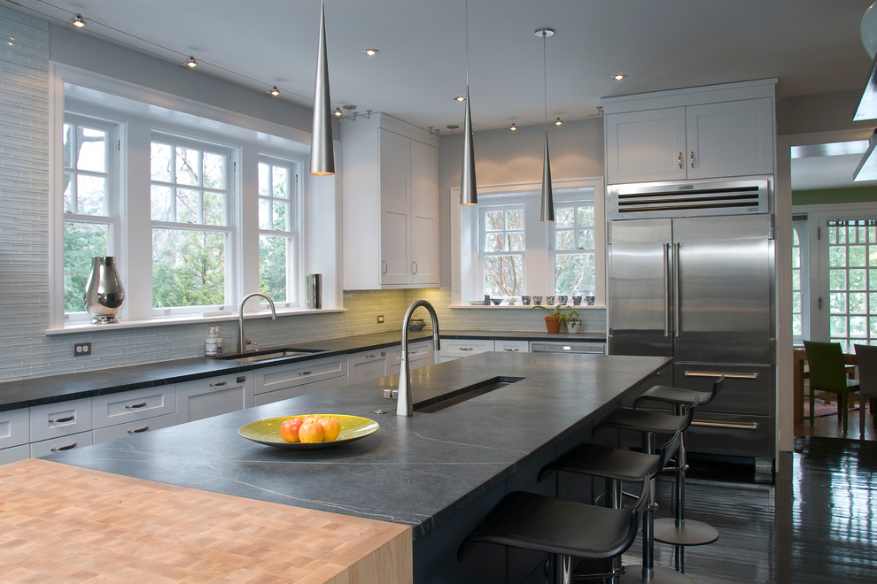 This is an example of a large contemporary eat-in kitchen in Philadelphia with white cabinets, white splashback, stainless steel appliances, glass tile splashback, with island, an undermount sink, soapstone benchtops, black benchtop and shaker cabinets.