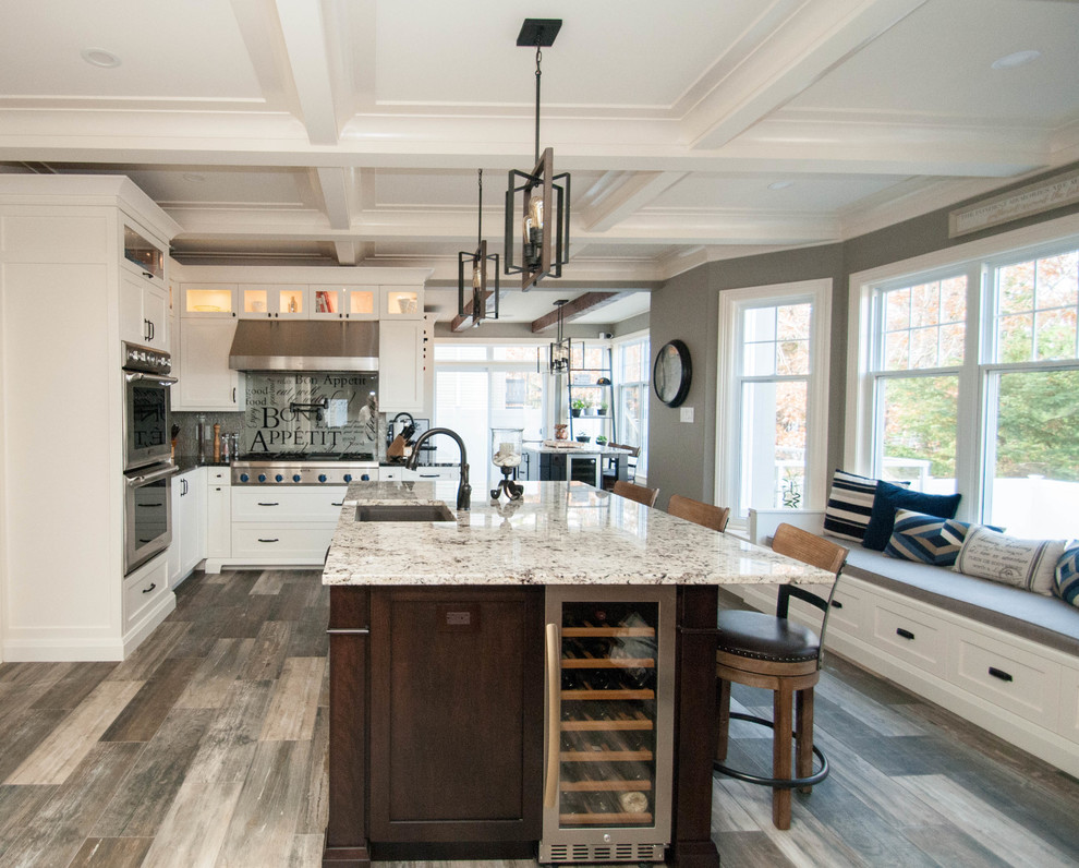 Large transitional l-shaped ceramic tile and brown floor kitchen photo with a farmhouse sink, shaker cabinets, white cabinets, granite countertops, gray backsplash, glass tile backsplash, paneled appliances, two islands and black countertops