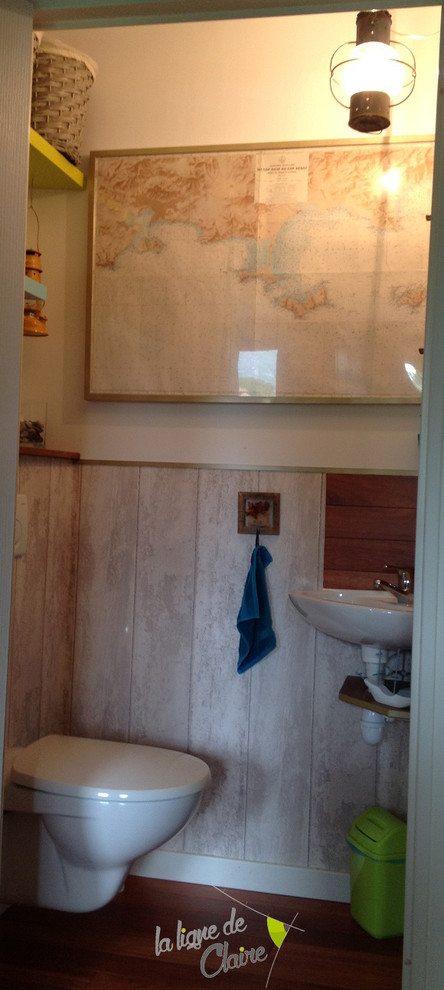 Small beach style powder room in Marseille with a wall-mount sink, wood benchtops, a wall-mount toilet and white walls.