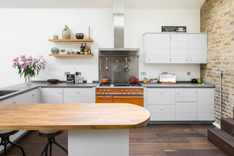 This is an example of a mid-sized contemporary u-shaped open plan kitchen in London with a drop-in sink, flat-panel cabinets, white cabinets, wood benchtops, grey splashback, stainless steel appliances, dark hardwood floors, brown floor and brown benchtop.