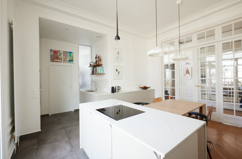 Cette photo montre une cuisine haussmannienne et grise et blanche moderne avec un évier encastré, des portes de placard beiges, une crédence blanche, un électroménager noir, un sol en carrelage de céramique, îlot, un sol gris et un plan de travail blanc.