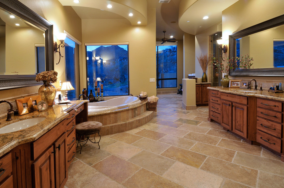 Photo of a large master bathroom in Phoenix with raised-panel cabinets, medium wood cabinets, a drop-in tub, beige walls, an undermount sink and brown floor.