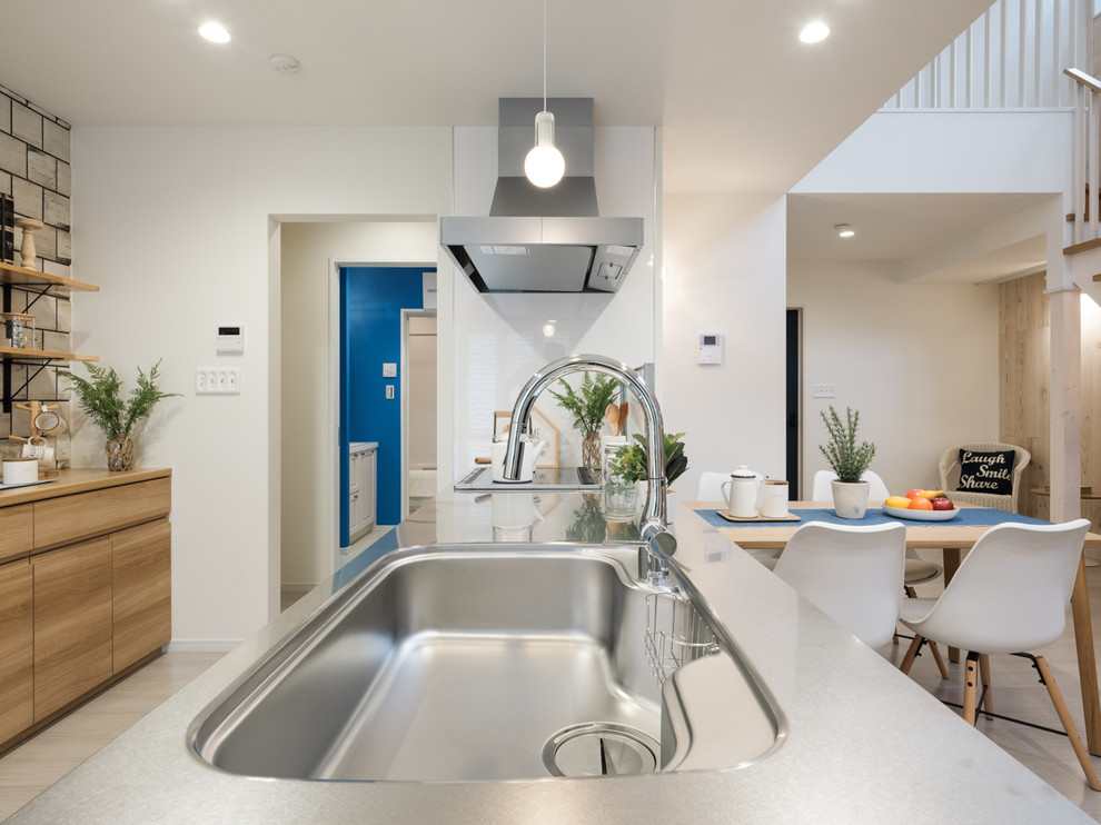 Beach style single-wall open plan kitchen in Other with a single-bowl sink, beaded inset cabinets, medium wood cabinets, stainless steel benchtops, white splashback, black appliances, plywood floors, beige floor and beige benchtop.
