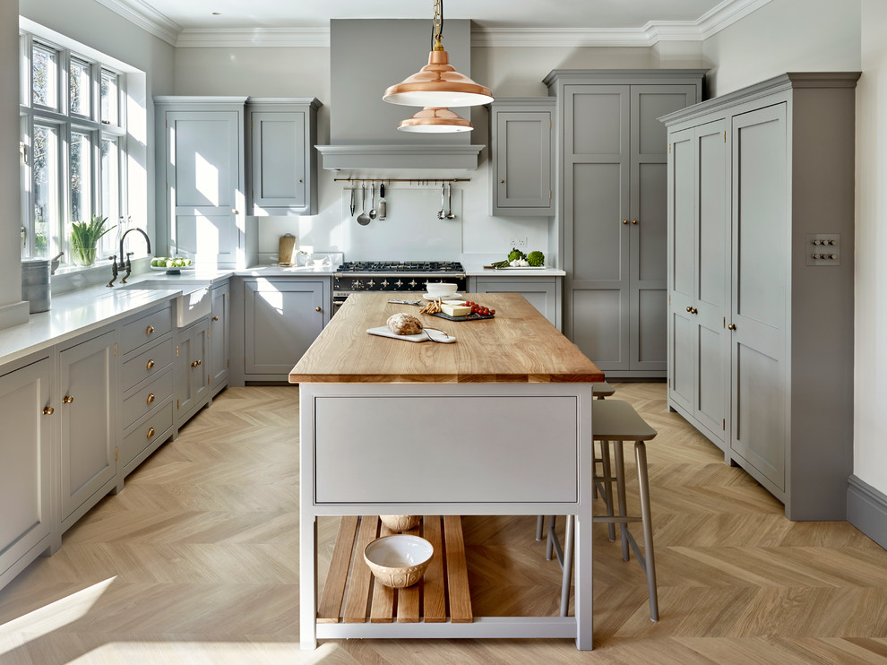 Transitional l-shaped eat-in kitchen in London with a farmhouse sink, shaker cabinets, grey cabinets, light hardwood floors and with island.