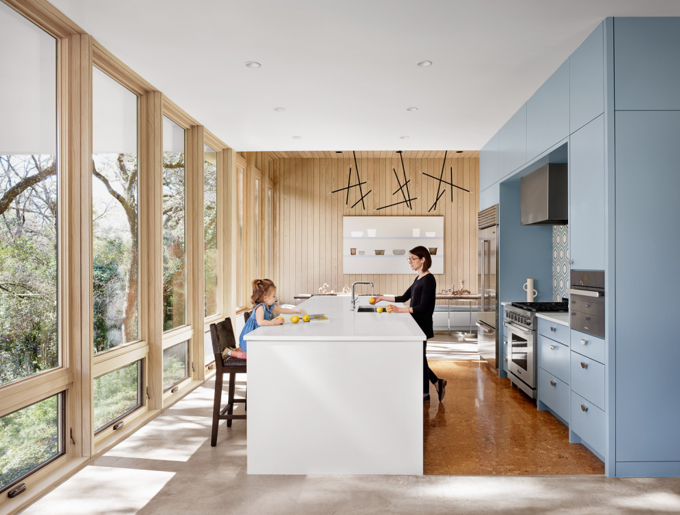 This is an example of a large midcentury galley open plan kitchen in Austin with an undermount sink, flat-panel cabinets, blue cabinets, quartz benchtops, multi-coloured splashback, cement tile splashback, stainless steel appliances, cork floors, with island, brown floor and white benchtop.