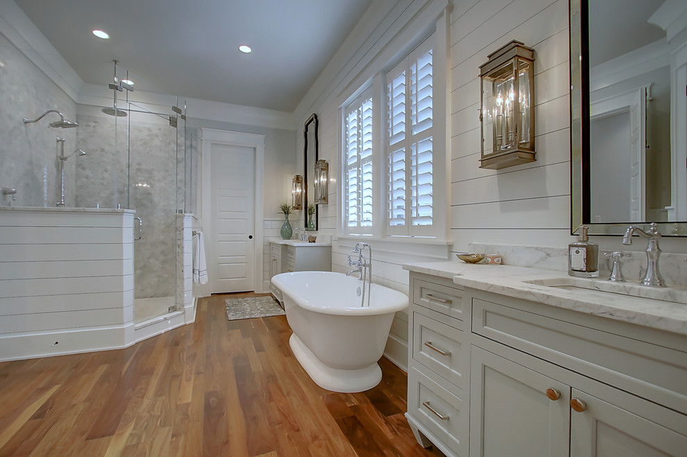 Large traditional master bathroom in Charleston with shaker cabinets, white cabinets, a freestanding tub, white tile, white walls, medium hardwood floors, an undermount sink, marble benchtops and a double shower.