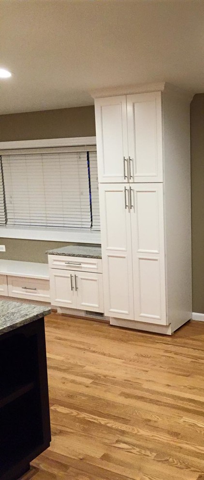 Example of a large transitional galley light wood floor open concept kitchen design in DC Metro with an undermount sink, recessed-panel cabinets, white cabinets, granite countertops, beige backsplash, white appliances and an island