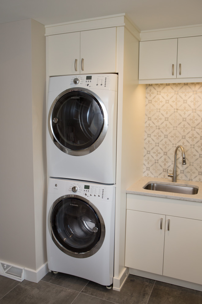 Design ideas for a large transitional l-shaped dedicated laundry room in Chicago with an undermount sink, flat-panel cabinets, white cabinets, quartz benchtops, multi-coloured walls, porcelain floors, a stacked washer and dryer, grey floor and grey benchtop.